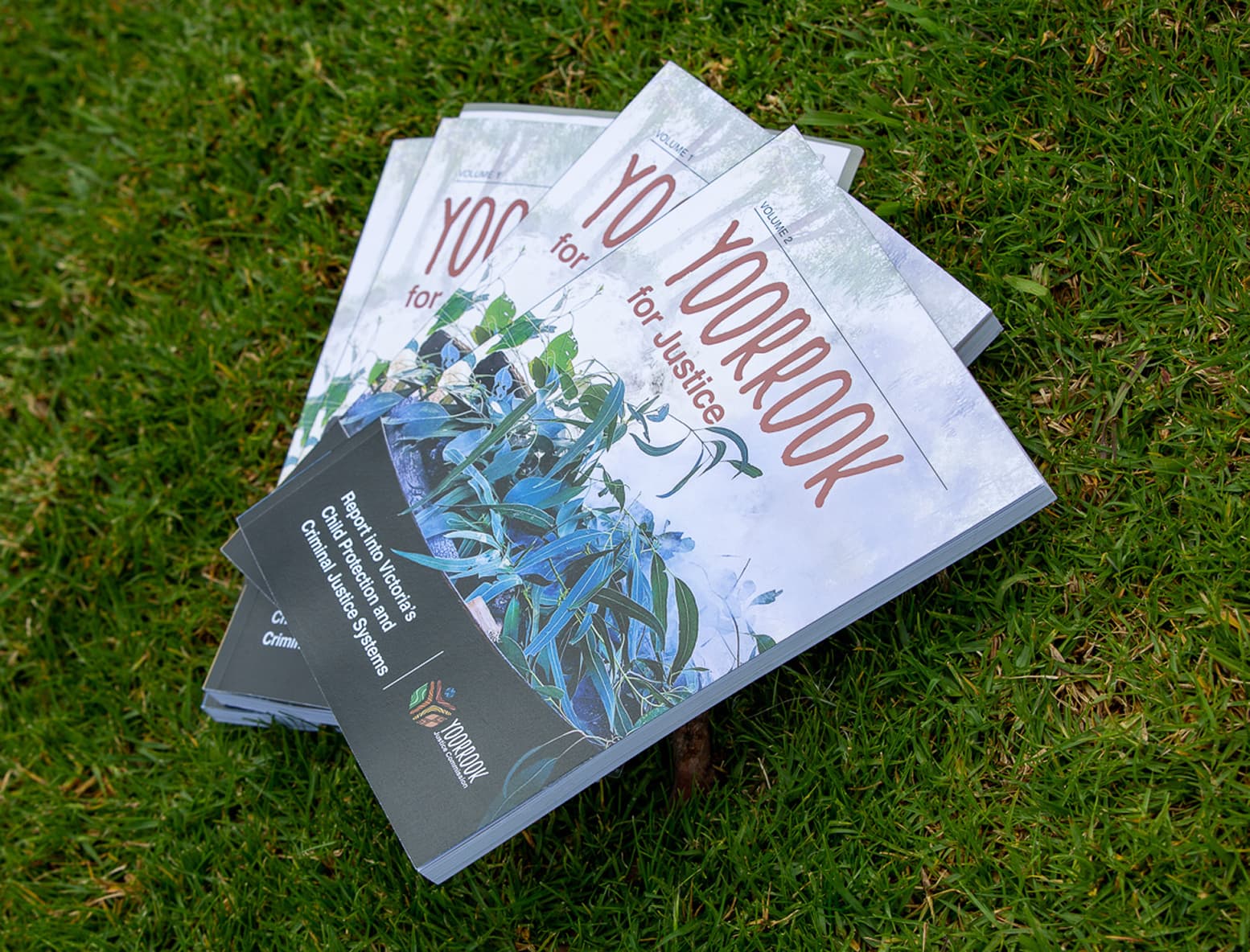 3 Yoorrook for Justice reports displayed on top of each other on a field of grass.