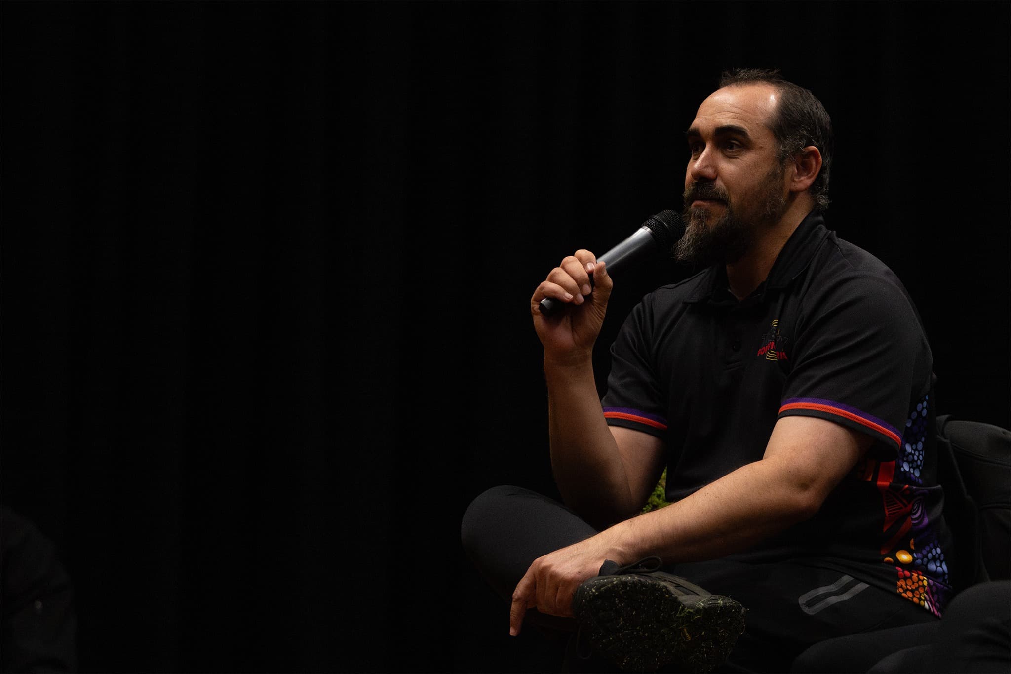 First Peoples Assembly Victoria Co-Chair Reuben Berg sits in chair while speaking into a microphone.