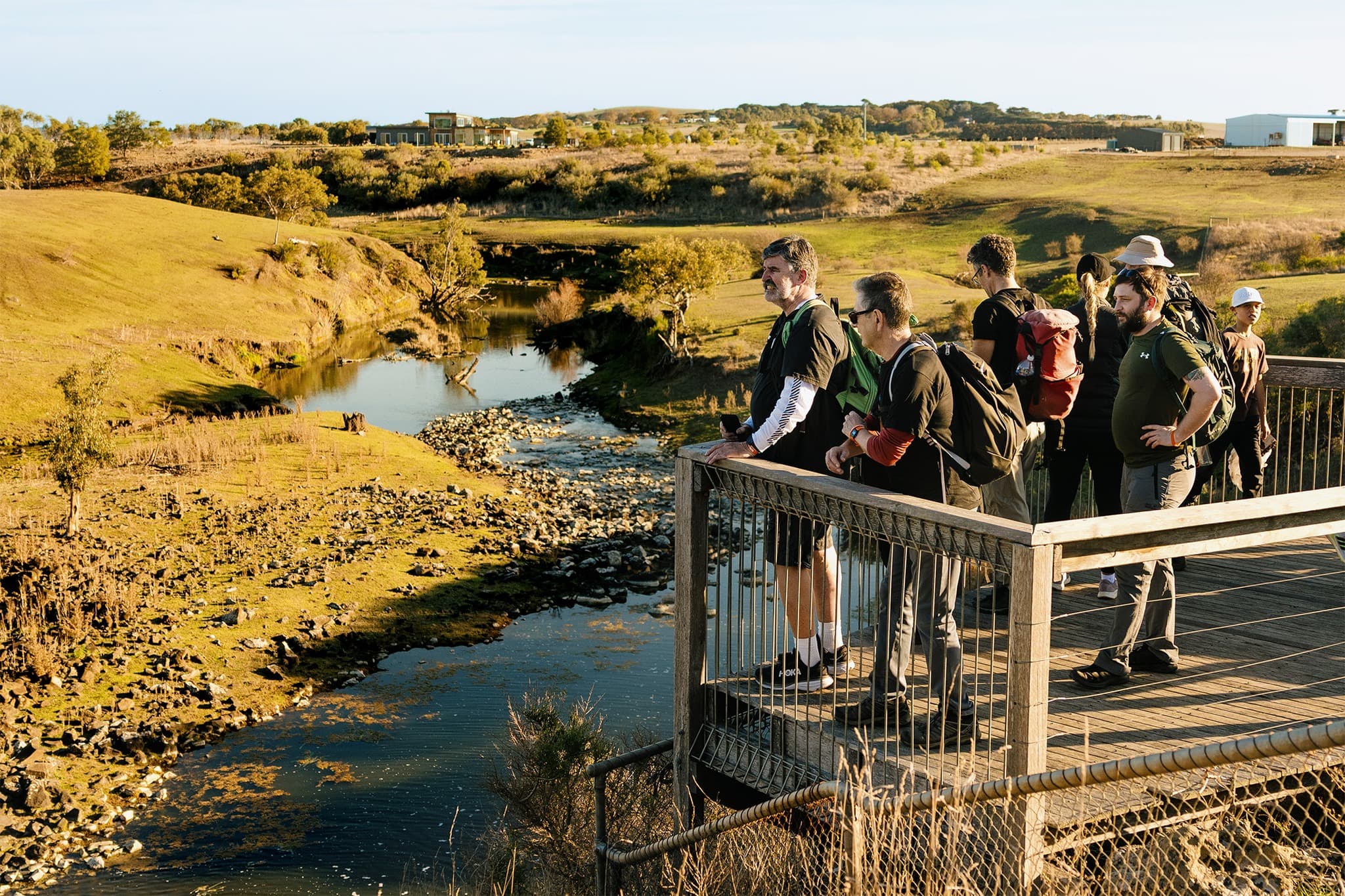 A group of people stand on a viewing platform overlooking a river surrounded by grassy fields.