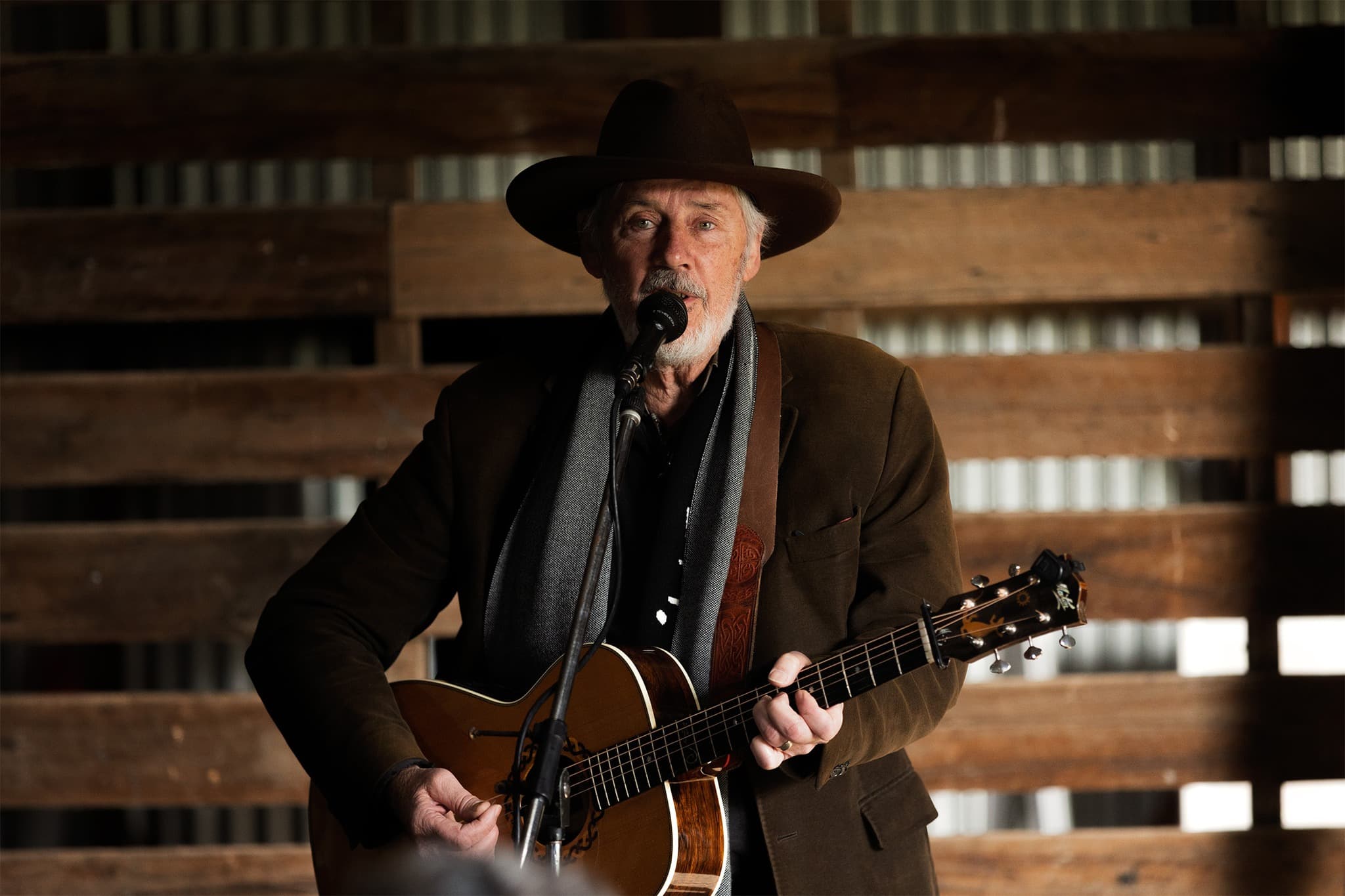Shane Howard singing into a microphone and playing a guitar indoors on the Walk for Truth