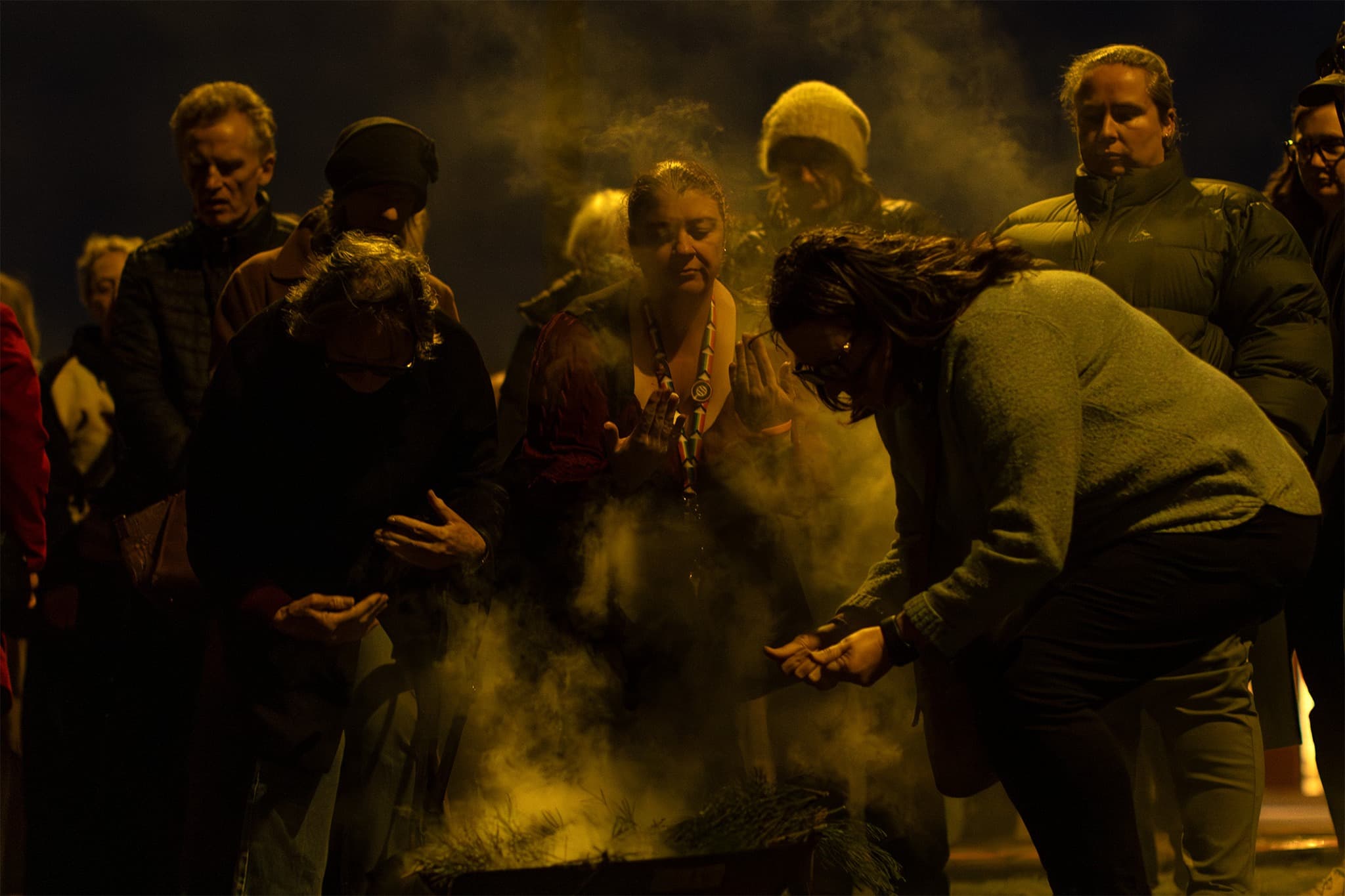 A group of people cleanse themselves in the smoke of an aboriginal smoking ceremony at a welcome to country along the Walk for Truth.