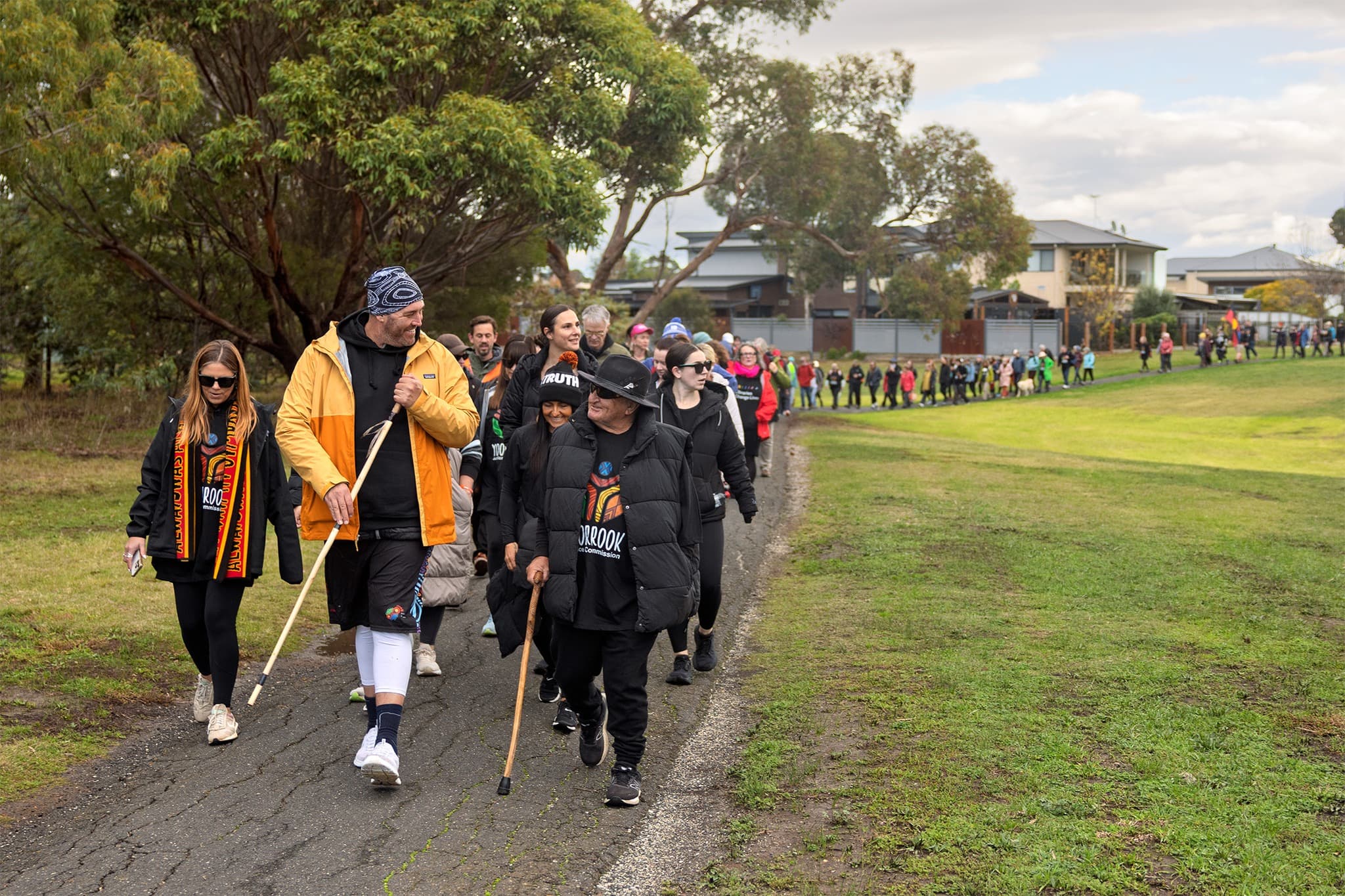 Commissioner Travis Lovett leads a long procession of people along a footpath surrounded by grass on one side and trees on the other on the Walk for Truth.