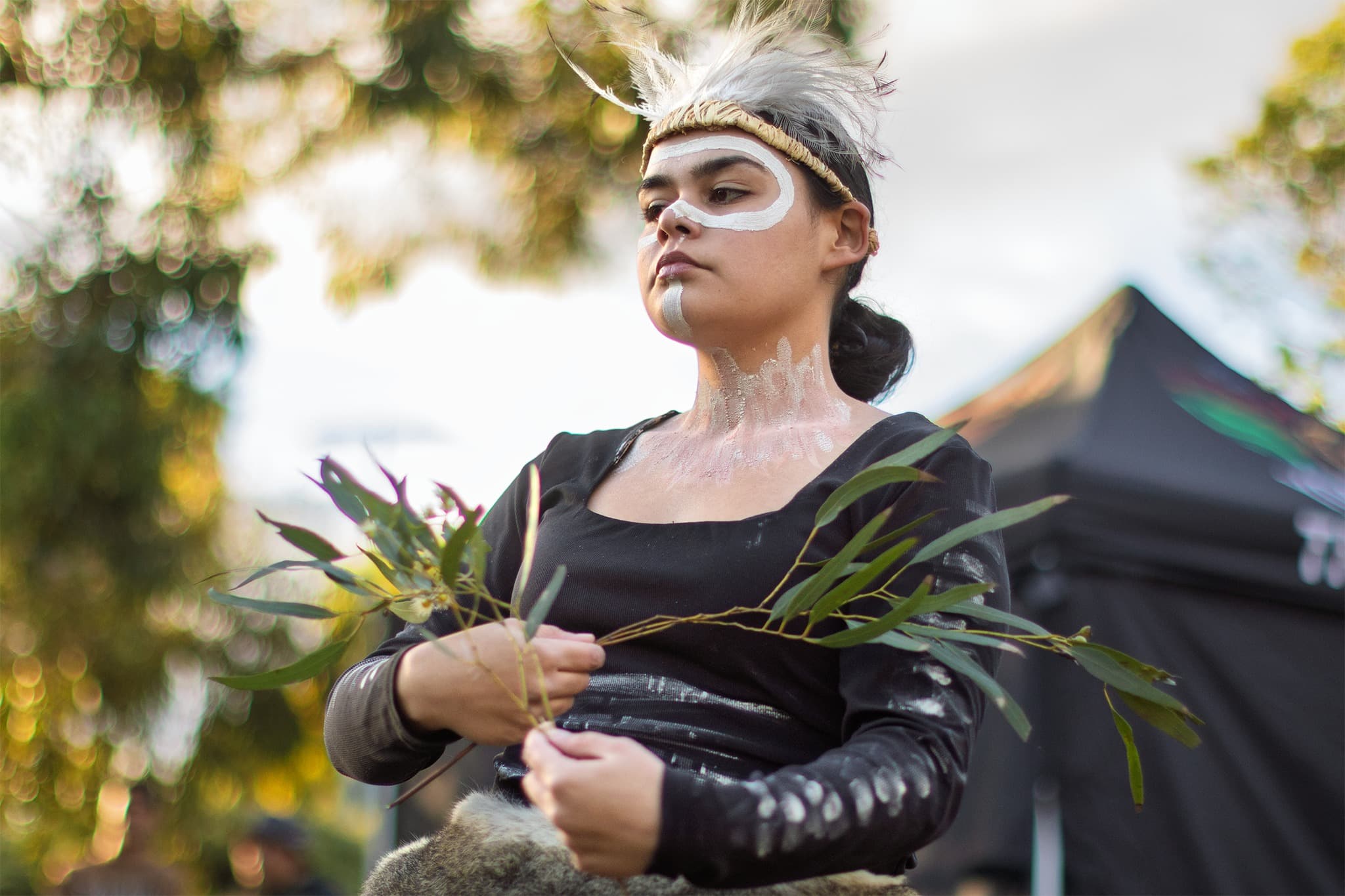 A woman from Nunkeri Tiddas dance group, in traditional aboriginal body paint, holds gum trees and performs a cultural dance on the Walk for tRUTH.