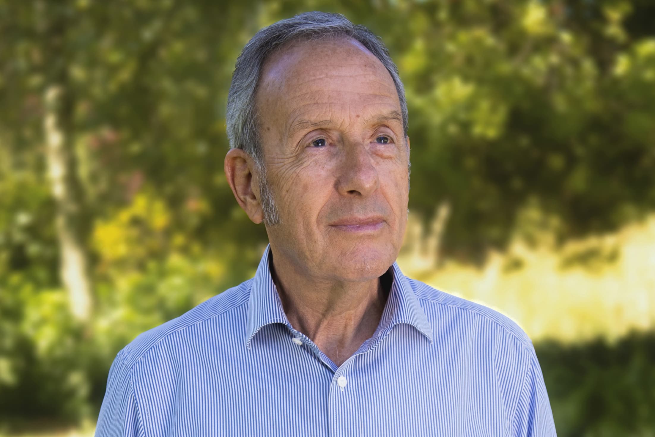 Headshot of Yoorrook Commissioner Tony North KC posing outdoors in a blue shirt.