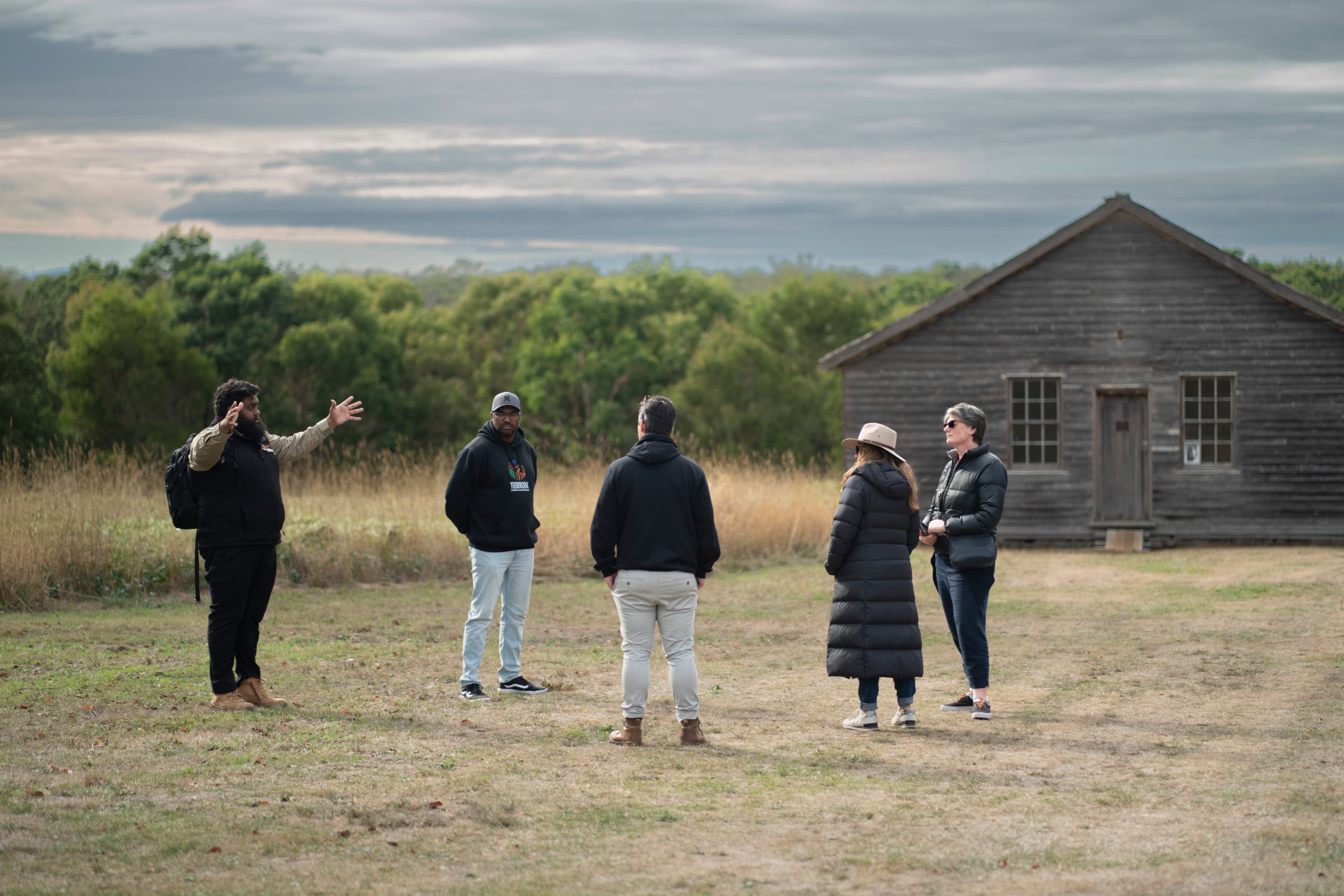 Braydon Saunders leads a tour for four Yoorrook staff members in an open field outside the historic dormitory at Lake Condah Mission.