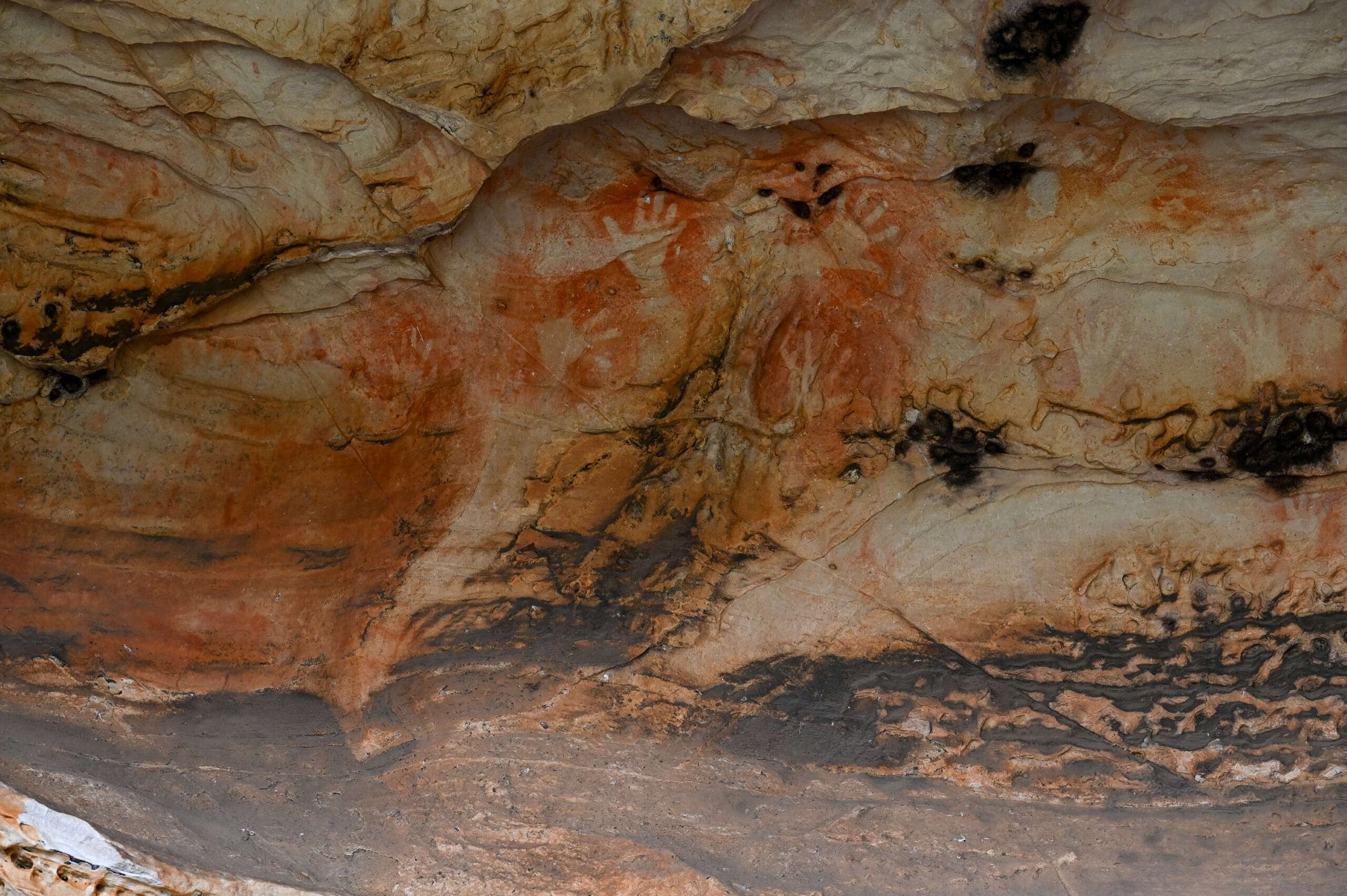 Rock art of hands outlined in orange ochre on a rocky overhang.