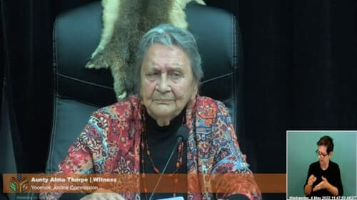 Aunty Alma Thorpe. seated in a black chair indoors at a Yoorrook public hearing.