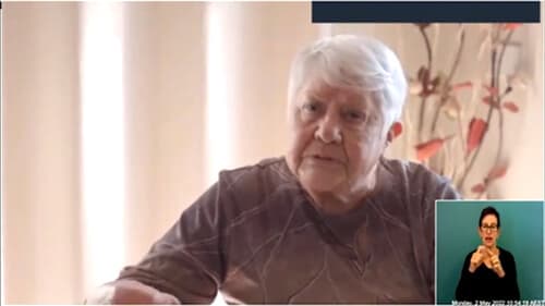 Aunty Fay Carter sits indoors with vertical blinds behind her; a sign language interpreter appears overlayed in the bottom right.