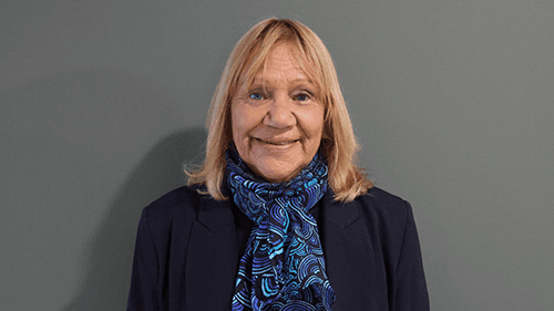 Aunty Geraldine Atkinson, smiling while standing in front of a grey wall.