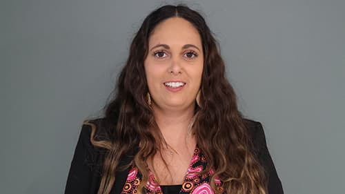 Bonnie Dukakis from Koorie Youth Council standing in front of a grey wall and smiling.
