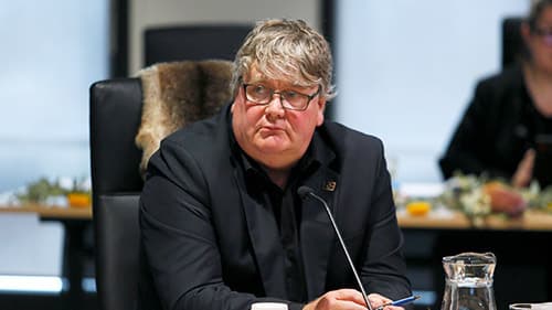 Darren Smith the CEO of Aboriginal Housing Victoria, seated in a black chair and wearing a black suit while he speaks into a microphone.