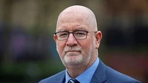 Dr. Darryl McGuire. wearing a blue suit and tie, is standing outdoors with a blurred background.