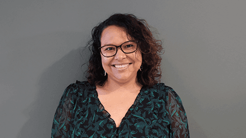 Dr Jacynta Krakouer from Monash University, smiling and standing in front of a grey wall.