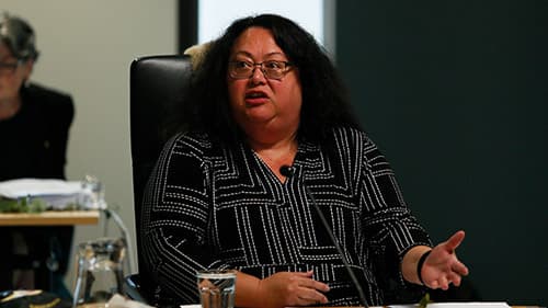 Lisa Briggs, Ngaweeyan Maar-oo, seated indoors on a black chair. She gestures with her left hand and talks into the microphone positioned in front of her.