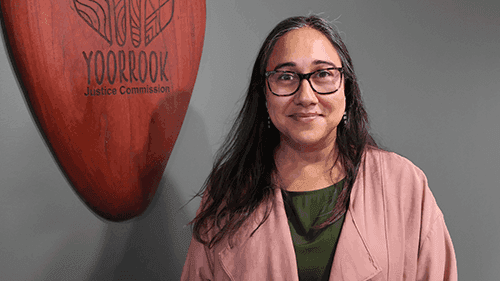 Commissioner Meena Sign standing in front of Yoorrook logo