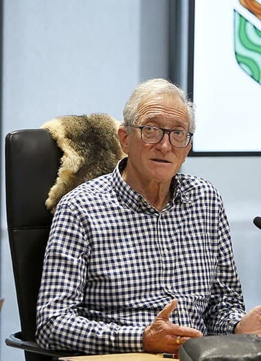 Emeritus Professor Richard Broome from La Trobe University, wearing a black and white checkered shirt, gestures with both hands at a Yoorrook public hearing.