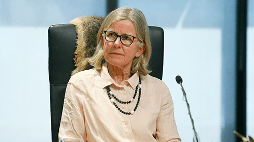 Elizabeth Balderstone dressed in a shirt and seated in front of a microphone at a Yoorrook public hearing.