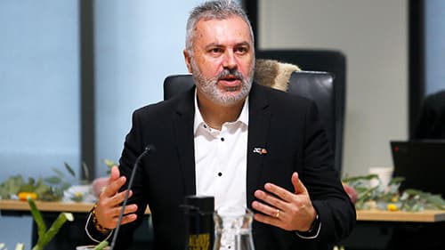 Michael Graham, Ngaweeyan Maar-oo, in a black suit, gestures with both hands while speaking towards a micrphone at a Yoorrook public hearing.