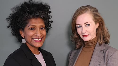 Anoushka Jeronimus and Melissa Hardham from West Justice stand side by side in front of a grey wall.